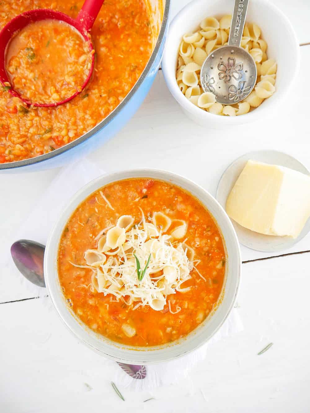 Chunky and Hearty Pinto Bean Soup in a white bowl, topped with parmesan cheese and pasta shells top view, with pot of soup in the background