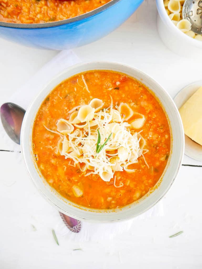 Chunky and Hearty Pinto Bean Soup in a white bowl, topped with parmesan cheese and pasta shells top view