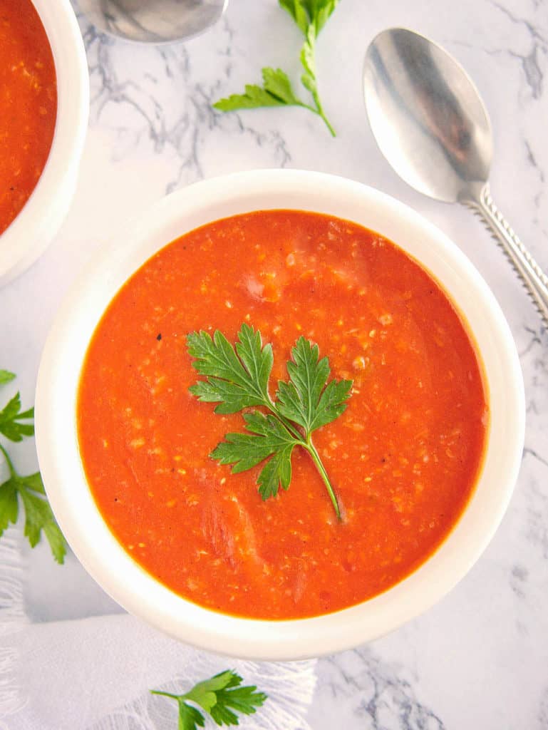 roasted vegan tomato soup topped with fresh herbs in a white bowl against a marble background, top view