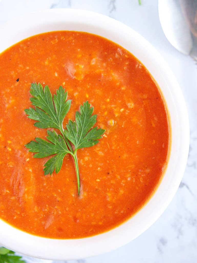roasted vegan tomato soup topped with fresh herbs in a white bowl against a marble background, top view