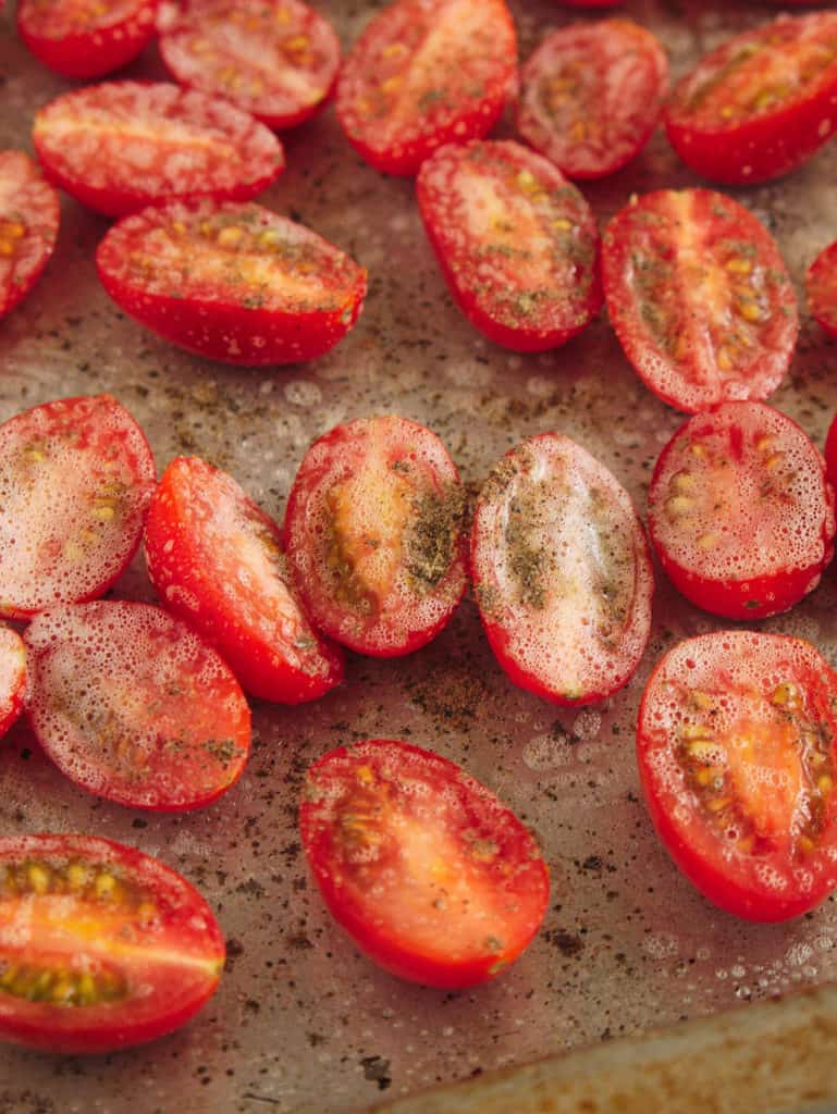grape tomatoes sliced on a baking sheet with salt/pepper