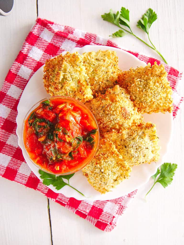 crispy air fryer ravioli with marinara sauce, served on a white plate with sauce on the side, top view