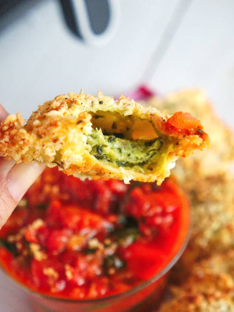 bite of crispy air fryer ravioli with marinara sauce, served on a white plate with sauce on the side
