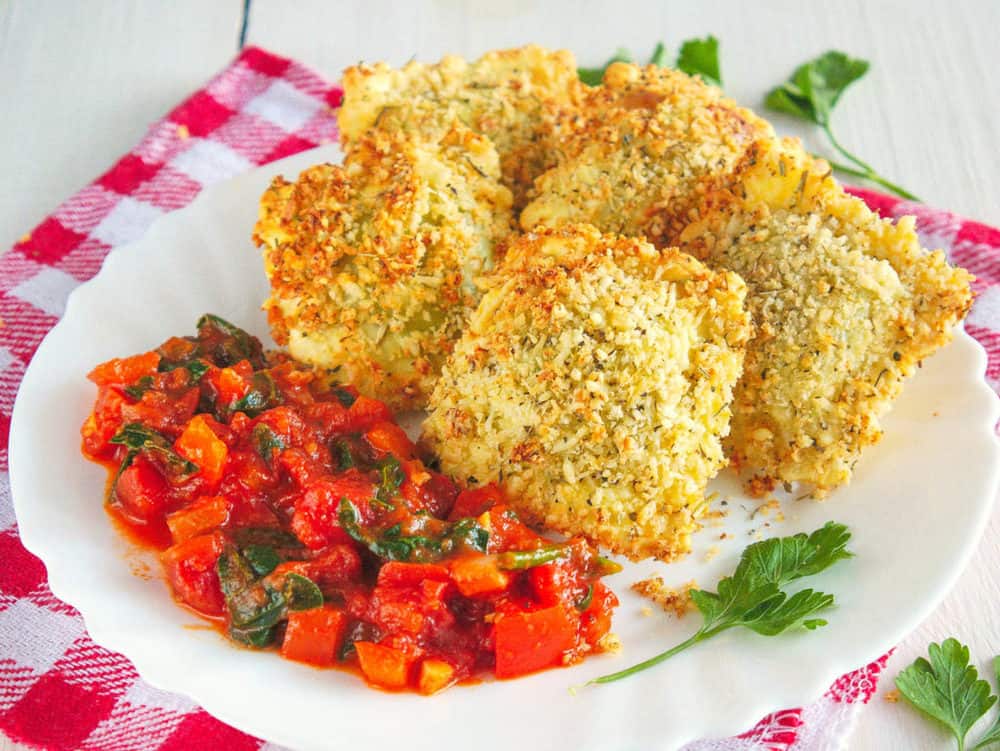 crispy air fryer ravioli with marinara sauce, served on a white plate with sauce on the side, side view
