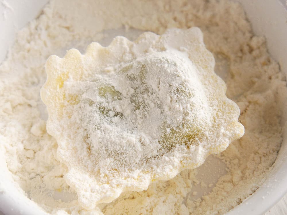 A white bowl filled with chickpeas and thyme sprigs on a tan surface in front of a green strainer with dry chickpeas.