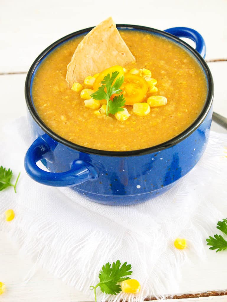 mexican corn soup - spicy, dairy-free, served in a blue bowl with fresh corn, tomatoes, and a corn chip as garnishes