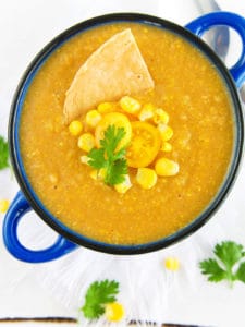 potato corn chowder - spicy, dairy-free, served in a blue bowl with fresh corn, tomatoes, and a corn chip as garnishes