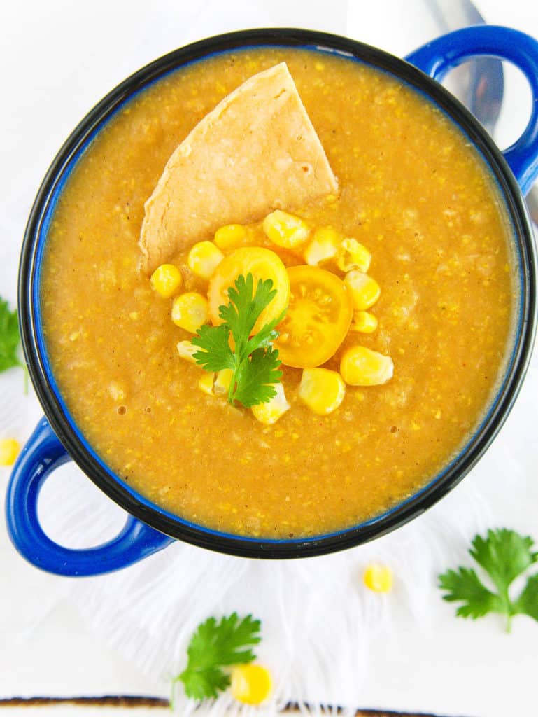 mexican corn soup - spicy, dairy-free, served in a blue bowl with fresh corn, tomatoes, and a corn chip as garnishes