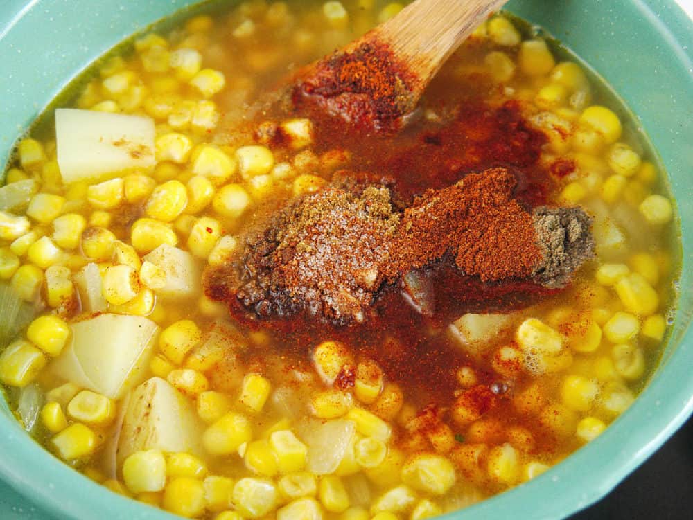 spices being added to pot with corn soup