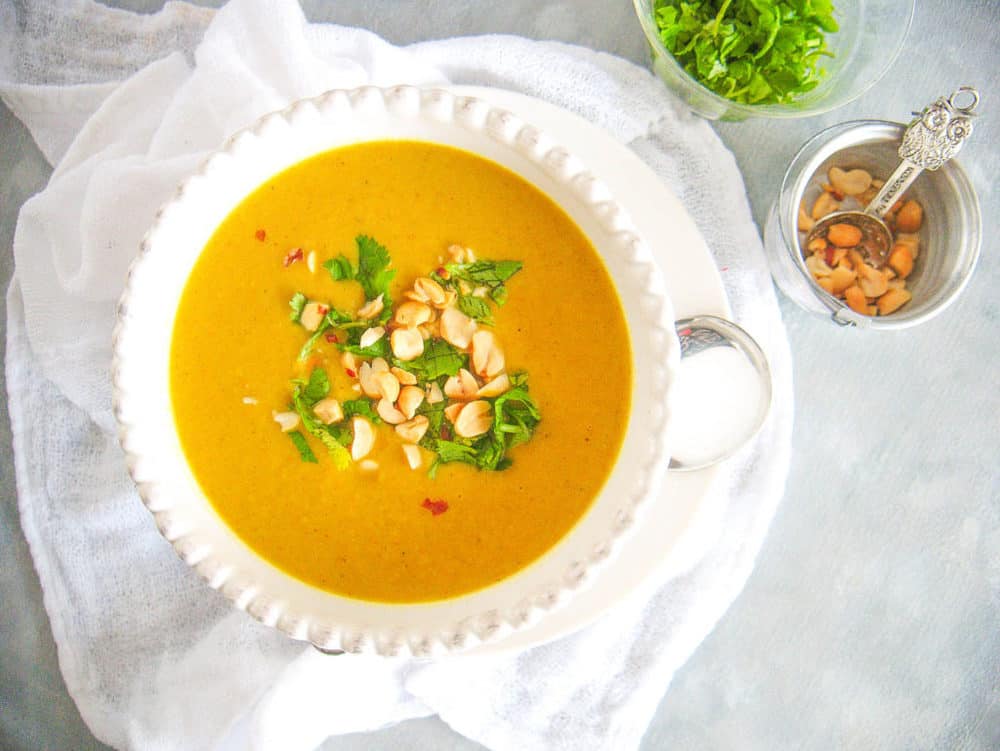 spicy cauliflower soup, topped with crushed cashews and cilantro, served in a white bowl