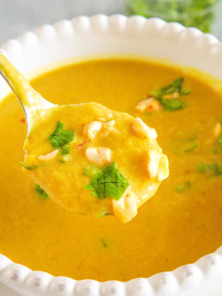 spoonful of spicy cauliflower soup, topped with crushed cashews and cilantro, served in a white bowl