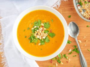 spicy sweet potato soup served in a white bowl, topped with crushed nuts and cilantro top view