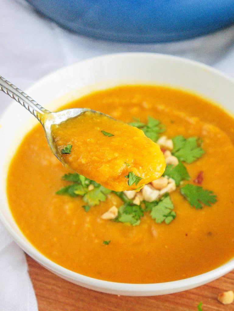 spoonful of spicy sweet potato soup served in a white bowl, topped with crushed nuts and cilantro