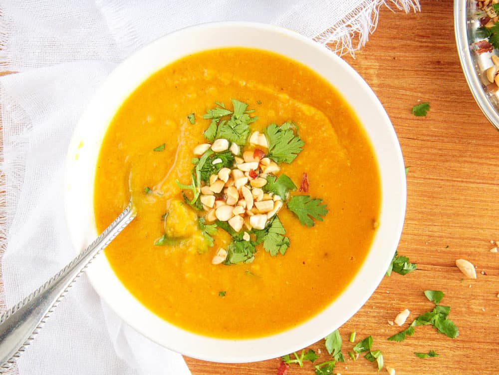 spicy sweet potato soup served in a white bowl, topped with crushed nuts and cilantro with spoon