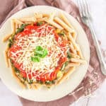 whole wheat pasta recipe topped with spinach, pasta sauce, parmesan cheese on a white plate, with a fork