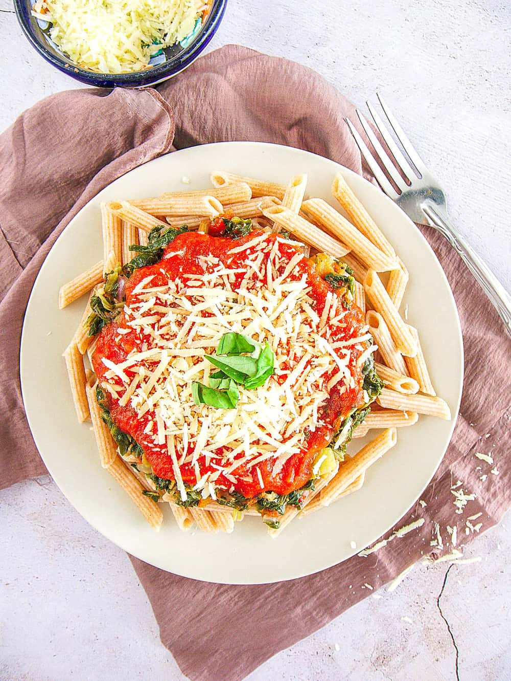 whole wheat pasta recipe topped with spinach, pasta sauce, parmesan cheese on a white plate, with a fork