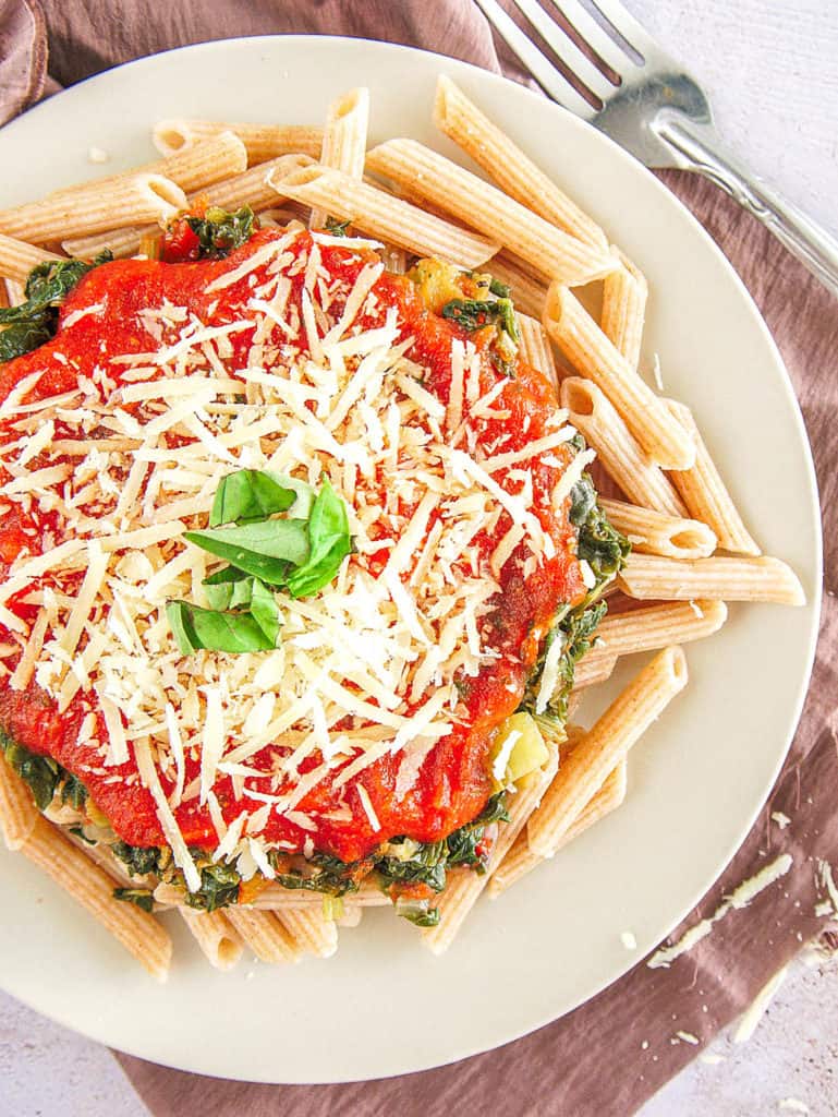 whole wheat pasta recipe topped with spinach, pasta sauce, parmesan cheese on a white plate, top view