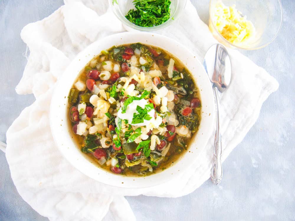 vegetarian black bean soup with kale and hominy, topped with sour cream and cilantro, served in a white bowl with a spoon, top view