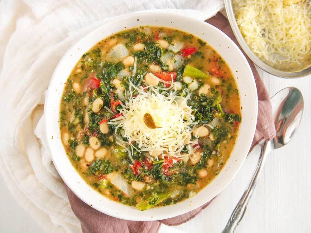 white bean and kale soup, served in a white bowl, topped with parmesan cheese - top view
