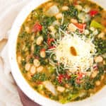 white bean and kale soup, served in a white bowl, topped with parmesan cheese - top view