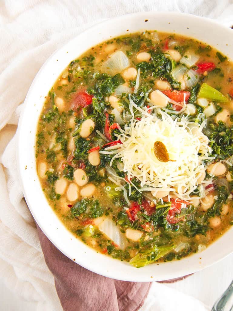 white bean and kale soup, served in a white bowl, topped with parmesan cheese - top view