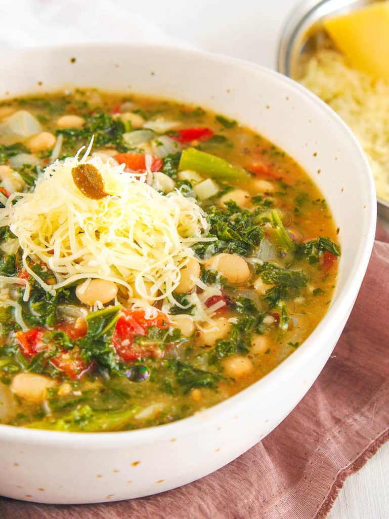 white bean and kale soup, served in a white bowl, topped with parmesan cheese - side view
