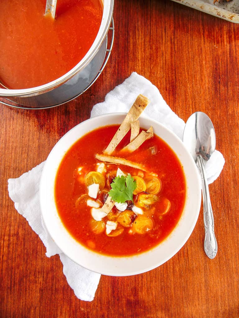 vegetarian taco soup served in a white bowl, topped with tomatoes goat cheese tortilla chips and cilantro with spoon on the side