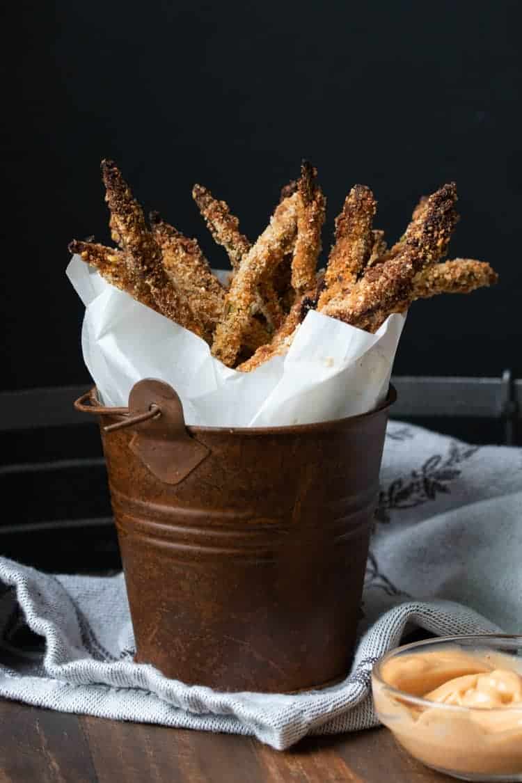 Crispy, crunchy, loved by the entire family and easy to throw together. This asparagus fries recipe makes the perfect side or stand alone snack! #veganappetizers #healthykidssnacks Crispy breaded asparagus fries wrapped in parchment in a brown bucket