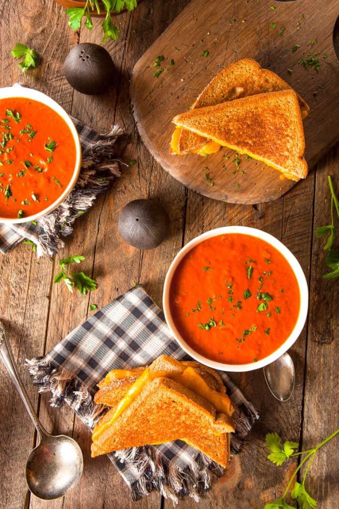 instant pot tomato soup pictured in a white bowl against a wooden background with a grilled cheese sandwich on the side