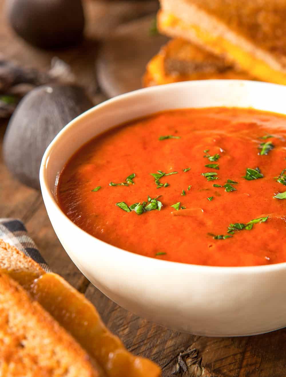 instant pot tomato soup pictured in a white bowl against a wooden background with a grilled cheese sandwich on the side