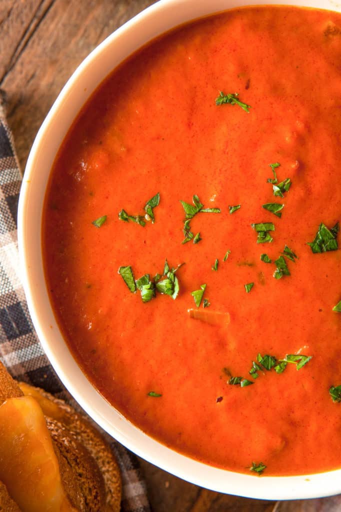 instant pot tomato soup pictured in a white bowl against a wooden background with a grilled cheese sandwich on the side