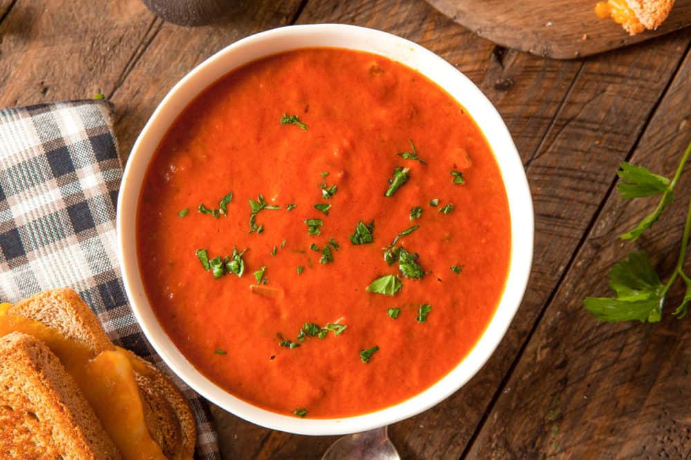 instant pot tomato soup pictured in a white bowl against a wooden background with a grilled cheese sandwich on the side
