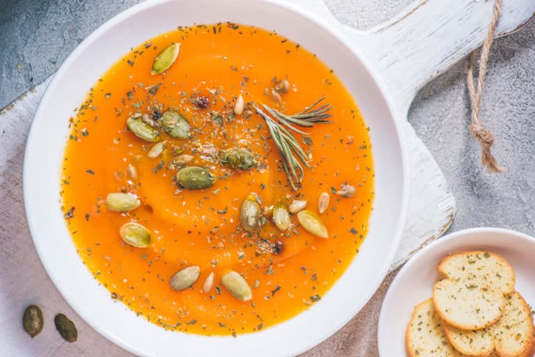 vegetarian white bean soup with pumpkin, served in white bowls, topped with pumpkin seeds