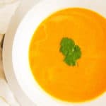 acorn squash bisque served in a white bowl with fresh herbs on top, top view