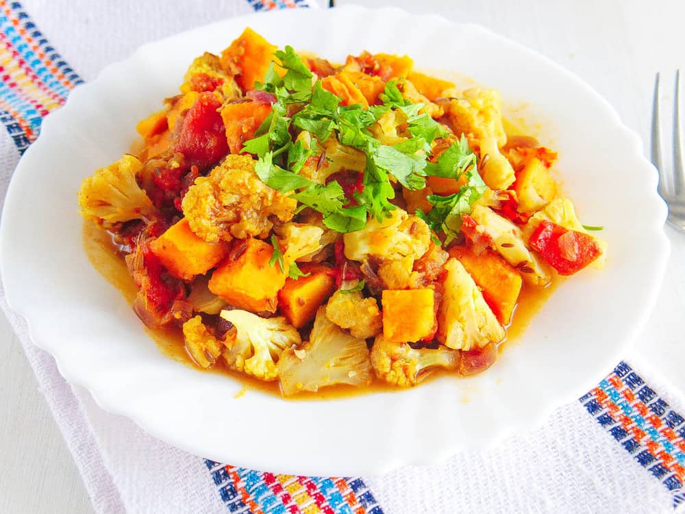 roasted cauliflower curry with sweet potatoes topped with cilantro, served on a white plate