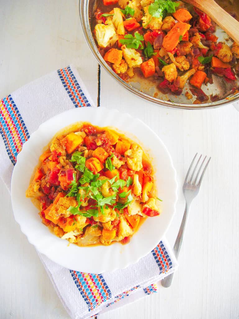 roasted cauliflower curry with sweet potatoes topped with cilantro, served on a white plate