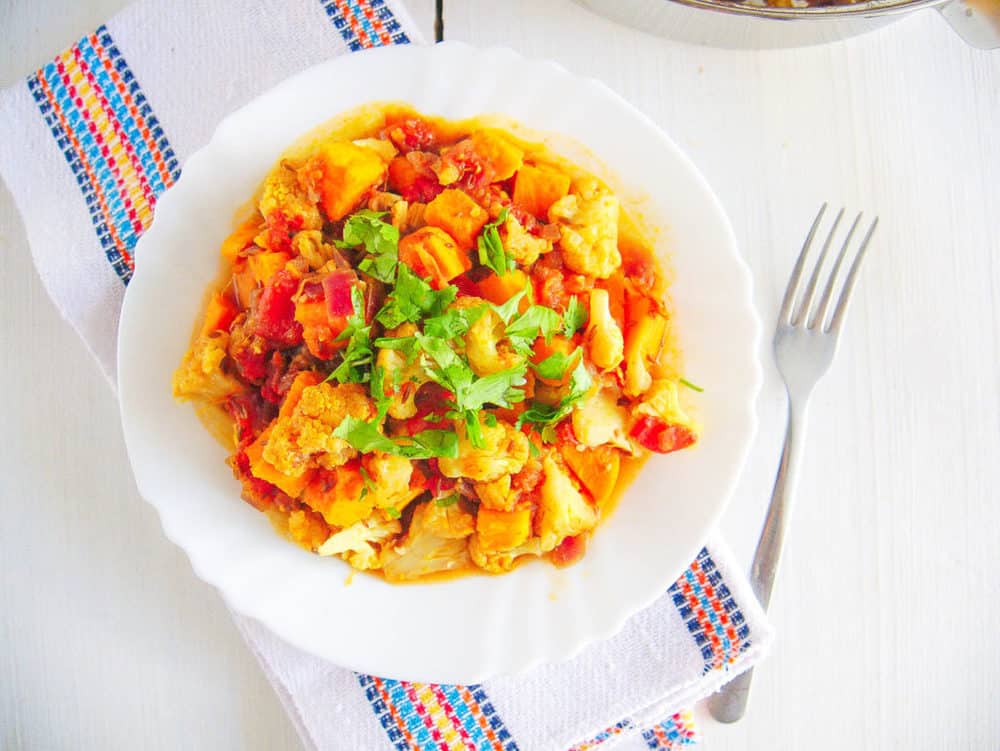 roasted cauliflower curry with sweet potatoes topped with cilantro, served on a white plate with a fork
