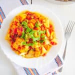 roasted cauliflower curry with sweet potatoes topped with cilantro, served on a white plate with a fork