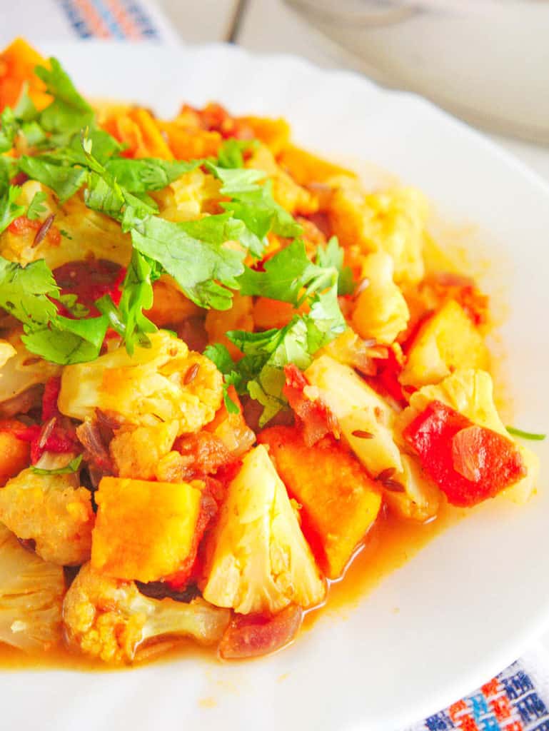 closeup of roasted cauliflower curry with sweet potatoes topped with cilantro, served on a white plate