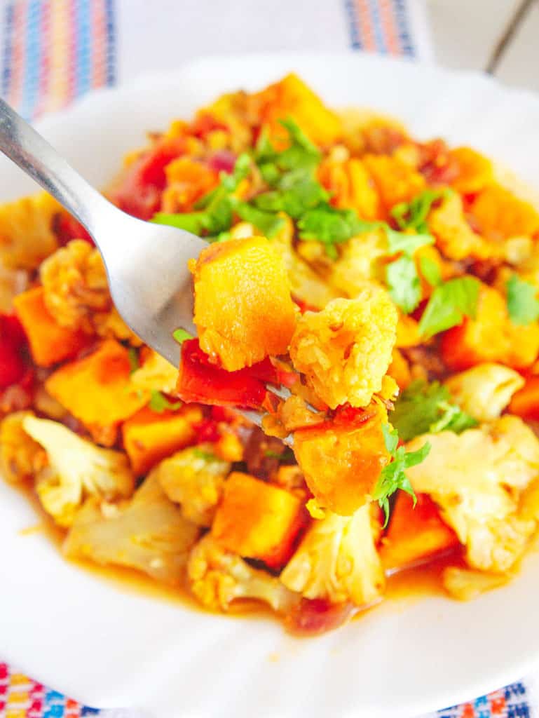forkful of roasted cauliflower curry with sweet potatoes topped with cilantro, served on a white plate