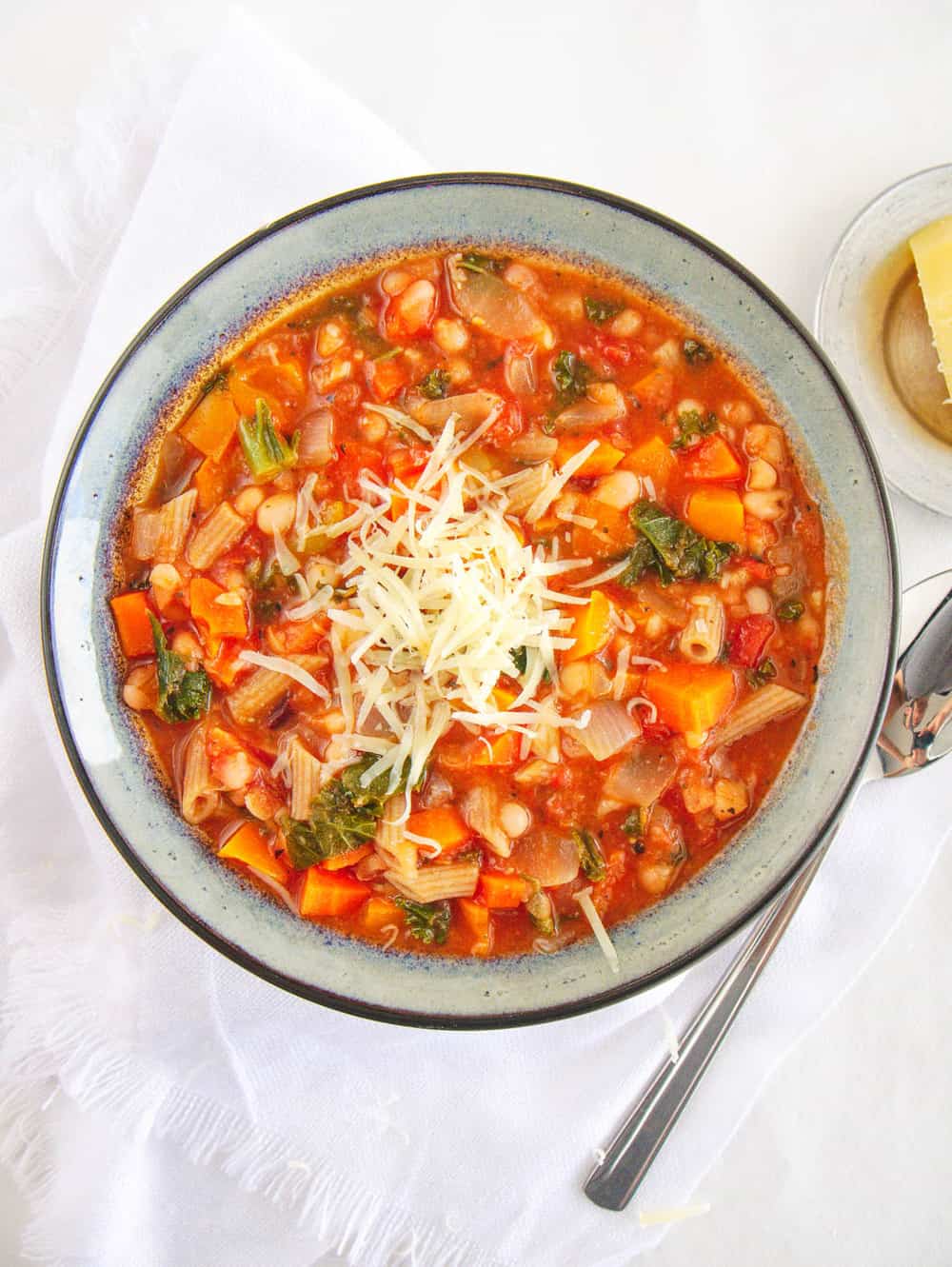 Tuscan Bean Stew with W،le Wheat Pasta, topped with parmesan cheese and served in a ceramic bowl