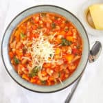 Tuscan Bean Stew with Whole Wheat Pasta, topped with parmesan cheese and served in a ceramic bowl