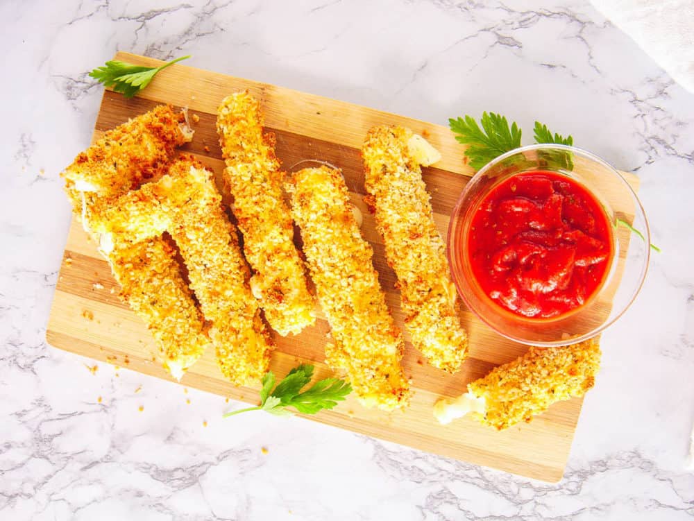 air fryer mozzarella sticks served on a wooden cutting board with tomato dipping sauce, top view