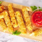 air fryer mozzarella sticks served on a wooden cutting board with tomato dipping sauce, top view