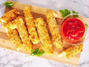 air fryer mozzarella sticks served on a wooden cutting board with tomato dipping sauce, top view