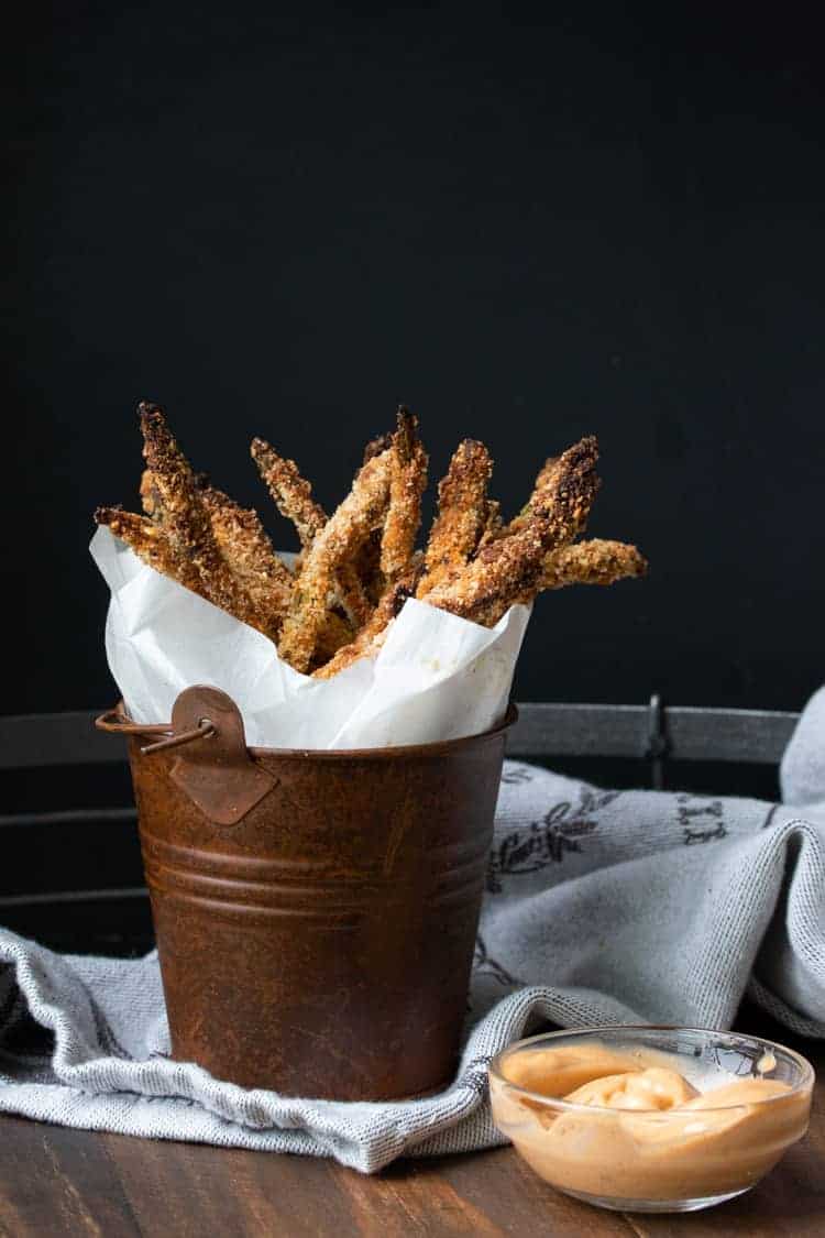 Crispy, crunchy, loved by the entire family and easy to throw together. This asparagus fries recipe makes the perfect side or stand alone snack! #veganappetizers #healthykidssnacks Brown bucket with parchment paper and breaded asparagus fries in it