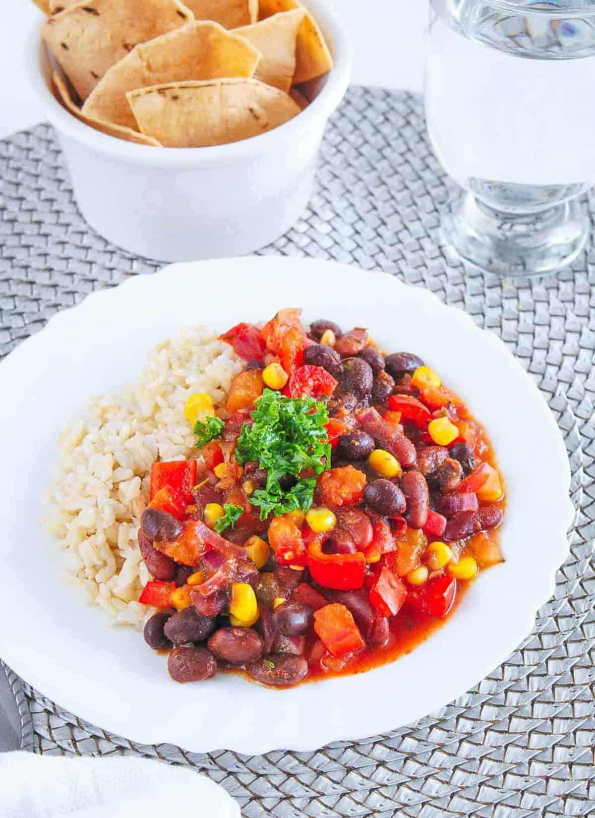 Rice and beans stew served on a white plate with chips and water on the side.