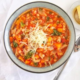 Tuscan bean stew topped with parmesan cheese and served in a ceramic bowl with a spoon.