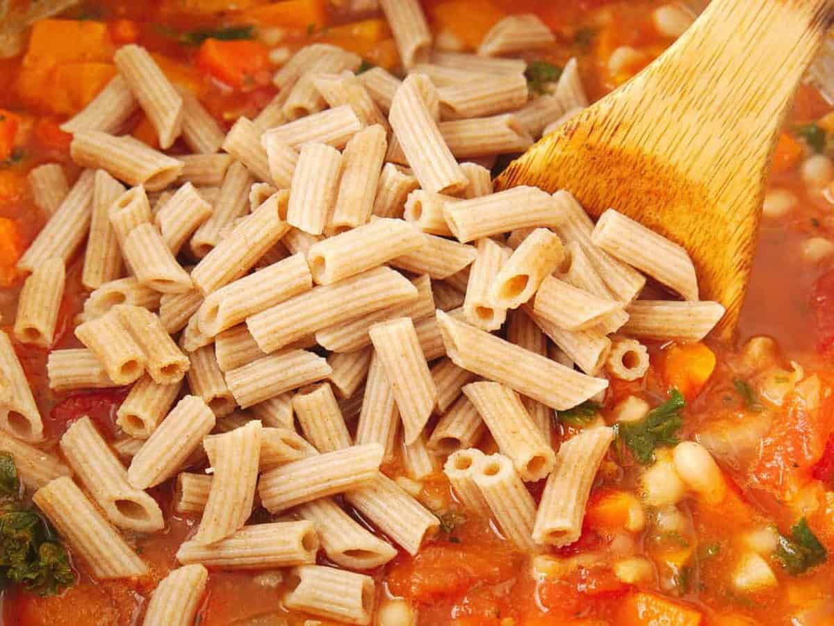 Whole wheat pasta added to a large pot with veggies, spices, and broth.