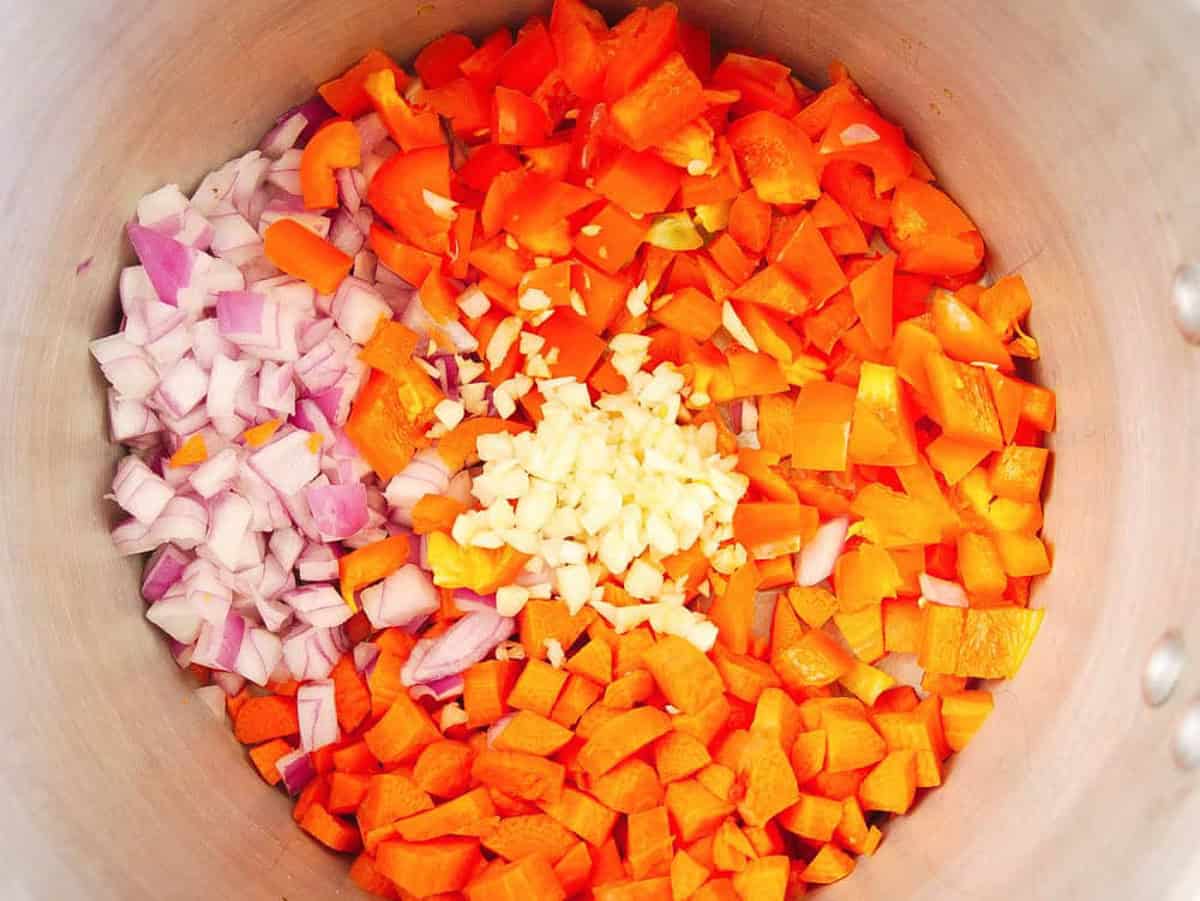 Onions, peppers, carrots, and garlic cooking in a pot on the stove.